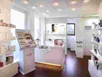 BABOR Aktiv Beauty Farm Heller Kosmetiksalon mit eleganten weißen Möbeln, Regalen voller Produkte und einem Bildschirm an der Wand.