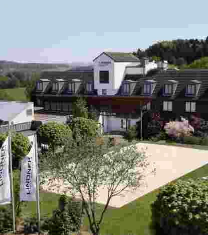 Aussenaufnahme Auf dem Bild ist das Lindner Hotel inmitten einer grünen, bewaldeten Landschaft unter blauem Himmel.