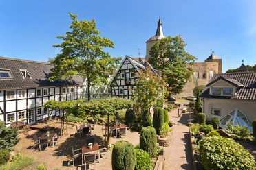 Außenansicht Ein idyllischer Innenhof mit Fachwerkhäusern, grüner Bepflanzung und einem historischen Kirchturm.