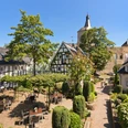 Außenansicht Ein idyllischer Innenhof mit Fachwerkhäusern, grüner Bepflanzung und einem historischen Kirchturm.
