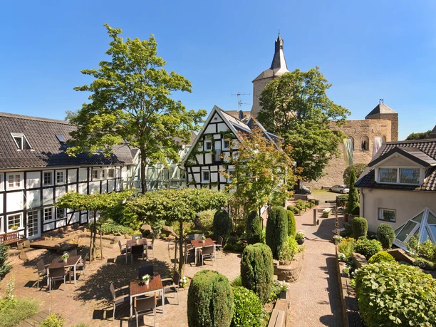 Außenansicht Ein idyllischer Innenhof mit Fachwerkhäusern, grüner Bepflanzung und einem historischen Kirchturm.
