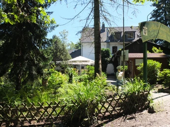 Haus Hardt Gemütlicher Garten eines Gasthofs mit Sonnenschirmen, umgeben von üppigem Grün und einem Holzzaun.