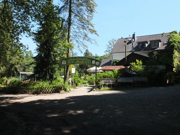 Haus Hardt Waldgasthaus mit überdachter Terrasse, umgeben von hohen Bäumen und dichter Vegetation.