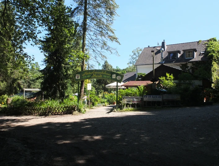 Haus Hardt Waldgasthaus mit überdachter Terrasse, umgeben von hohen Bäumen und dichter Vegetation.