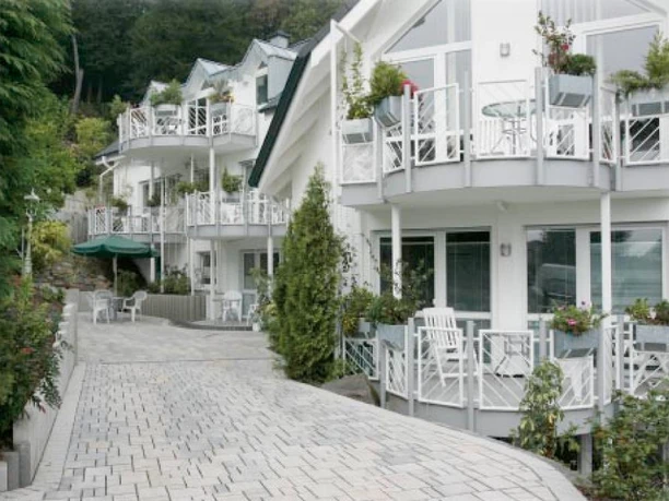 Pension Waldesruh Mehrstöckige, weiße Gebäude mit Balkonen, umgeben von grünen Pflanzen und gepflastertem Weg.