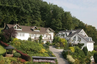 Eine Pension im Grünen mit gepflegtem Garten und traditionellen weißen Gebäuden, umgeben von Wald.