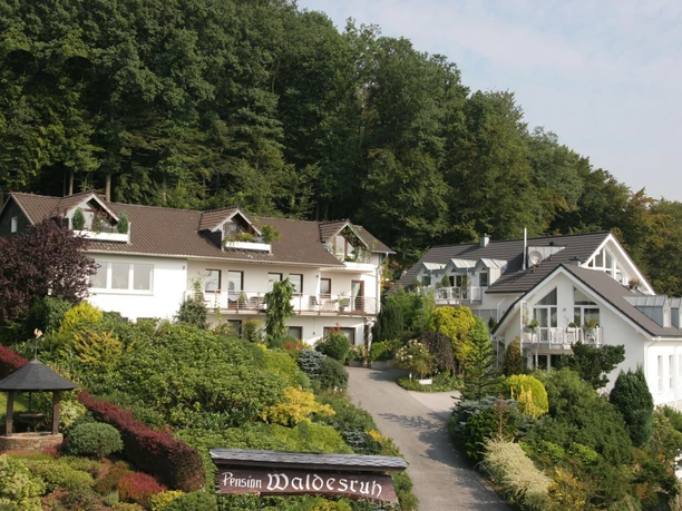 Pension Waldesruh Eine Pension im Grünen mit gepflegtem Garten und traditionellen weißen Gebäuden, umgeben von Wald.
