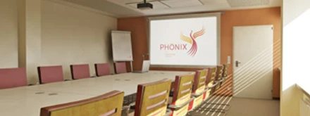 Seminarraum Moderner Konferenzraum mit langem Tisch und rosa-gelben Stühlen, Leinwand mit Phönix-Logo.