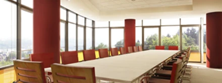Tagungsraum Moderner Konferenzraum mit großem Tisch, roten Stühlen und Panoramafenstern mit Waldblick.