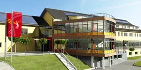 Aussenansicht Modernes, gelbes Gebäude mit Glasfront und Fahne davor, auf leicht ansteigendem, begrüntem Gelände.