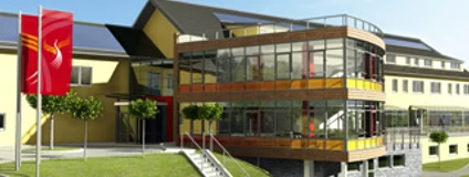 Aussenansicht Modernes, gelbes Gebäude mit Glasfront und Fahne davor, auf leicht ansteigendem, begrüntem Gelände.