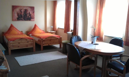 Zimmer Ein gemütliches Gästezimmer mit zwei Einzelbetten, einem Tisch, vier Stühlen und warmen Farbakzenten.