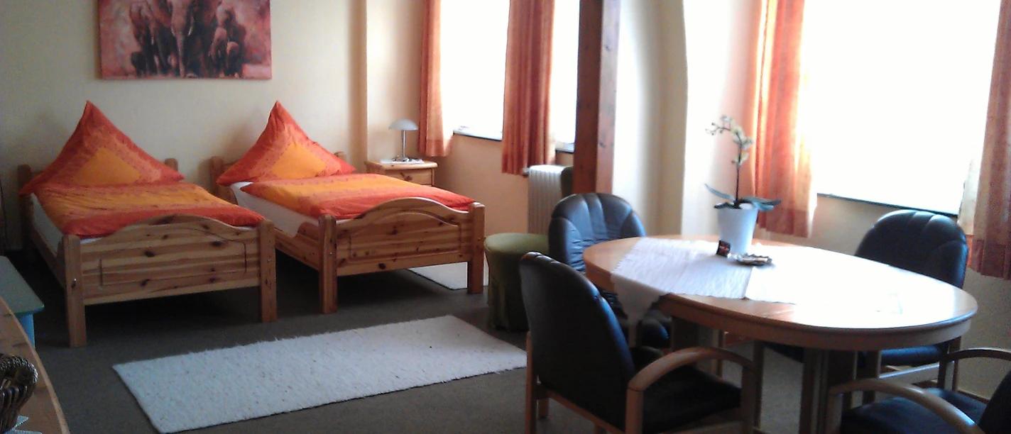 Zimmer Ein gemütliches Gästezimmer mit zwei Einzelbetten, einem Tisch, vier Stühlen und warmen Farbakzenten.