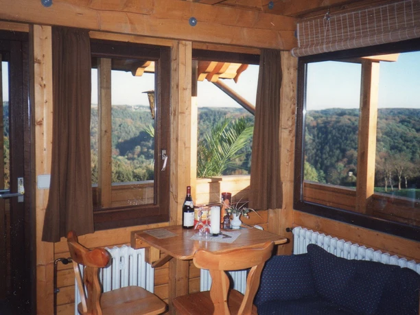 Zimmer Rustikaler Holztisch in gemütlichem Raum mit Panoramablick auf grüne, bewaldete Hügel im Hintergrund.