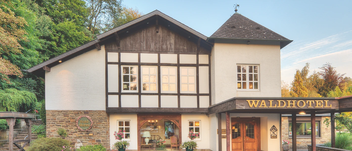 Waldhotel Mangold Traditionelles Fachwerkhotel in idyllischer Umgebung, umgeben von grünen Bäumen und Natur.