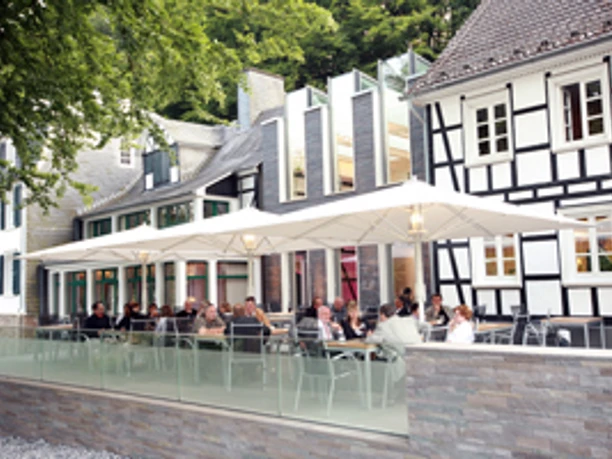 Seminar- und Tagungshotel Große Ledder mit Außenterrasse Ein modernes Fachwerkhaus mit einer Terrasse voller Menschen, die unter großen weißen Schirmen sitzen.