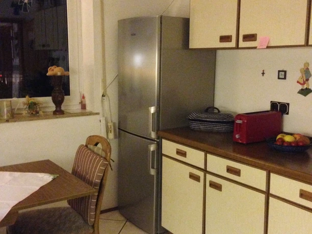 Vila Chopin Gemütliche Küche mit Holztisch, Stühlen, Kühlschrank und Schränken, warm beleuchtet, heimisches Ambiente.