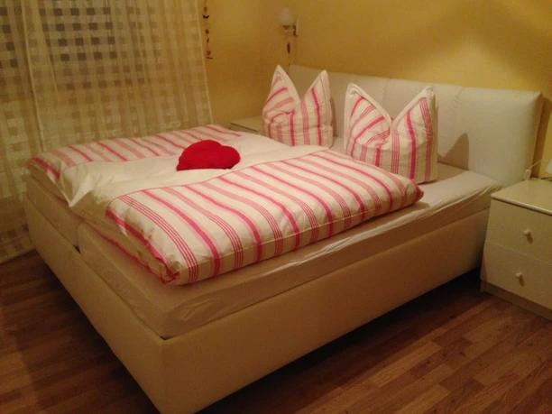 Vila Chopin Doppelbett in gelbem Raum mit rosa-weiß gestreifter Bettwäsche und zwei Herz-Kissen, Holzfußboden.