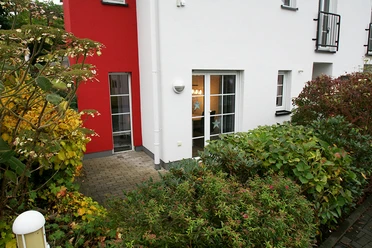 Außenansicht Mehrfamilienhaus mit weißer und roter Fassade, umgeben von herbstlicher Bepflanzung.