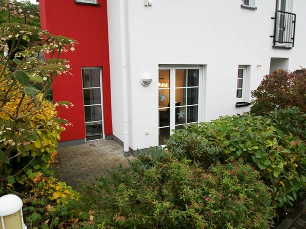 Außenansicht Mehrfamilienhaus mit weißer und roter Fassade, umgeben von herbstlicher Bepflanzung.