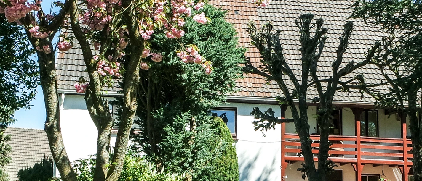 Hoffmanns Hof Zweistöckiges weißes Haus mit rotem Balkon, umgeben von blühenden Kirschbäumen und grünem Rasen.