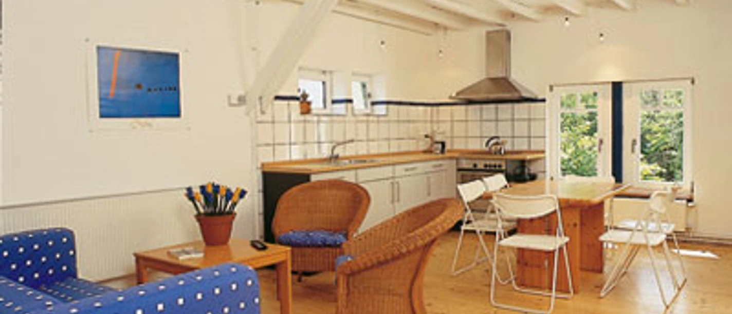 Wohnbereich Helles Wohnzimmer mit Holzboden, Esstisch mit weißen Stühlen, blauer Couch und Rattan-Sesseln.