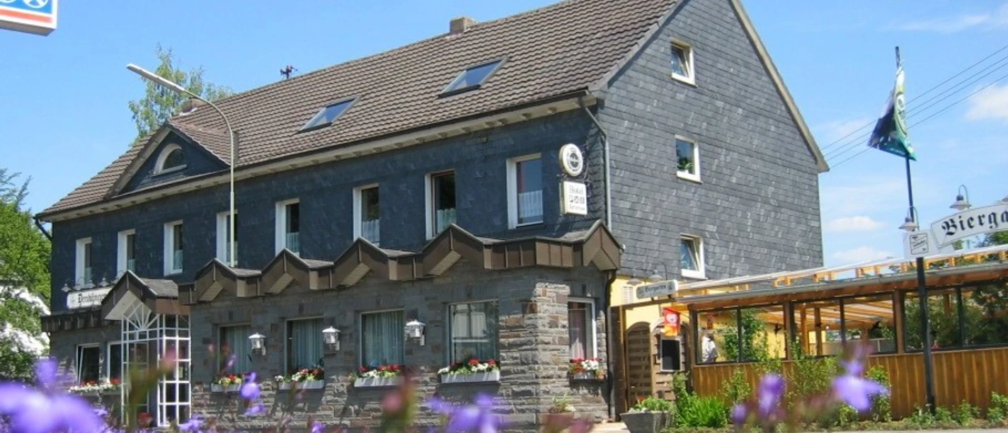 Außenansicht Traditionelles Gasthaus mit Schieferfassade, blauen Blumen im Vordergrund und Sommerhimmel im Hintergrund.