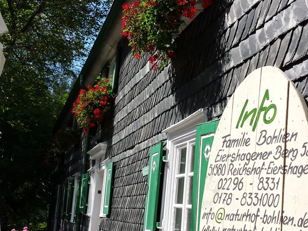 Naturhof Bohlien Schieferverkleidetes Fachwerkhaus mit grünen Fensterläden und blühenden Blumenkästen.