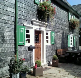 Naturhof Bohlien Historisches Fachwerkhaus mit Schieferfassade, grünen Fensterläden und blühenden Geranien.