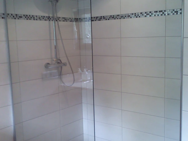 Naturhof Bohlien Dusche mit Glastrennwand, Regendusche und schwarz-weiß gefliestem Boden in modernem Design.