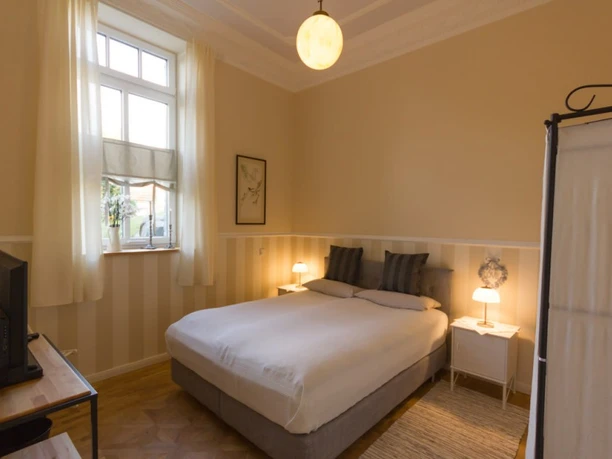 Villa Ruth - Wohnung 6 Schlafzimmer Helles, gemütliches Schlafzimmer mit Doppelbett, Nachttischen, Fenster und dezenten Dekorationen.