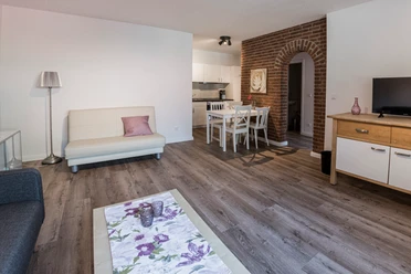 Essecke mit offener Küche Heller Wohnbereich mit Sofa, weißem Esstisch, offener Küche und einem markanten Backsteinbogen.