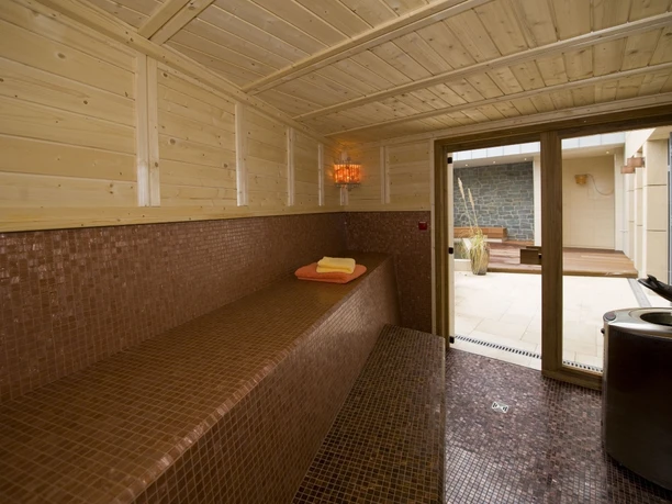 Wellnessbereich mit holzgetäfelten Wänden, Liegebank und Zugang zur Terrasse mit Whirlpool im Freien.