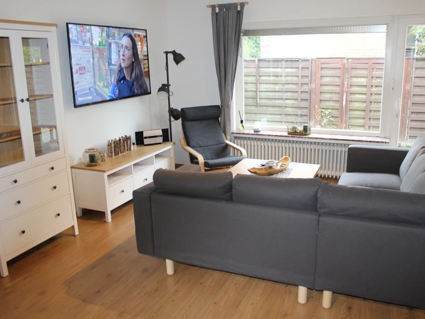 Bei Pohls Ein moderner Wohnbereich mit grauem Sofa, Sessel, Flachbildschirm und großen Fenstern.