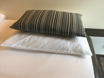 Two pillows, one striped and one white, lie on a bed with a white sheet.