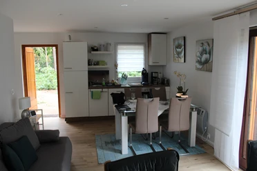 Een uitnodigende woonkamer met eettafel, open keuken en grote ramen voor veel natuurlijk licht.