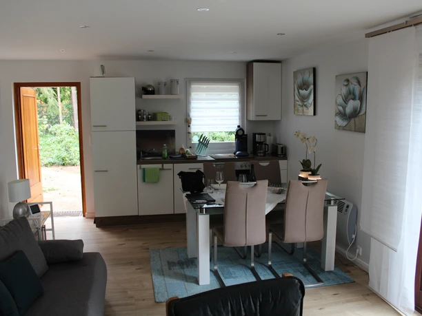 Een uitnodigende woonkamer met eettafel, open keuken en grote ramen voor veel natuurlijk licht.