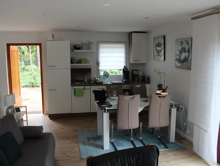 Ein einladendes Wohnzimmer mit Esstisch, offener Küche und großen Fenstern für viel Tageslicht.An inviting living room with dining table, open kitchen and large windows for plenty of natural light.En indbydende stue med spisebord, åbent køkken og store vinduer, der giver masser af naturligt lys.Een uitnodigende woonkamer met eettafel, open keuken en grote ramen voor veel natuurlijk licht.