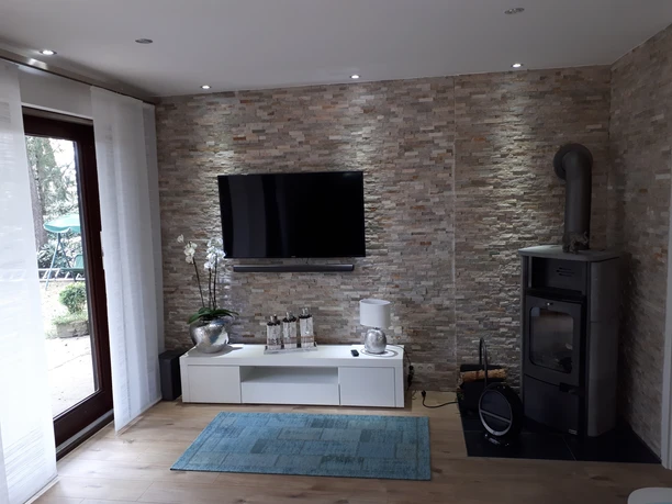 Moderne woonkamer met natuurstenen muur, flatscreen tv, houtkachel en elegante inrichting.