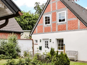 Rotes Backsteinhaus mit weißem Putz, umgeben von üppigem Grün in einem ruhigen Garten.