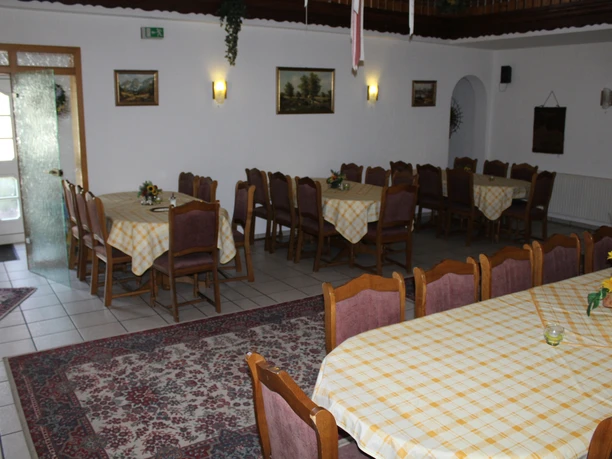 Ferienhof Meyer Ein heller Versammlungsraum mit mehreren Tischen, gelb karierten Tischdecken und rustikalen Holzmöbeln.