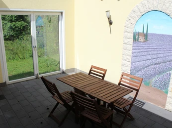 Ferienwohnung Reuter Eine Terrasse mit Holzmobiliar, einer großen Fensterfront und einer Wandmalerei im mediterranen Stil.