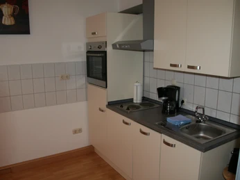 Kompakte Küchenzeile in einer Ferienwohnung mit Herd, Spüle, Kaffeemaschine und Oberschränken.