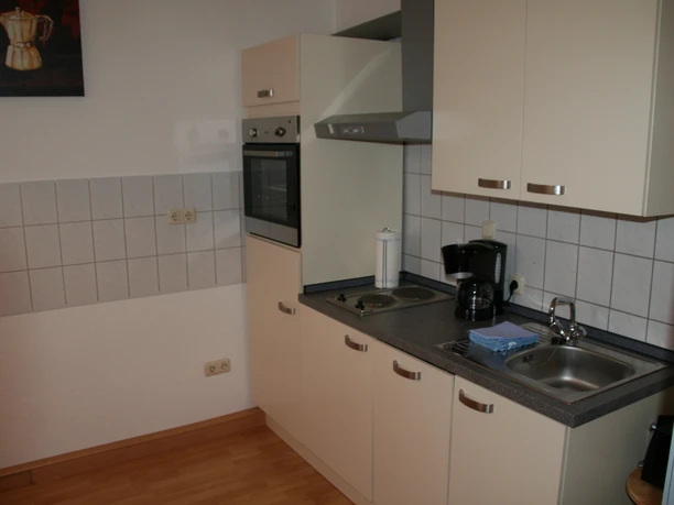 Compact kitchenette in a vacation apartment with stove, sink, coffee machine and wall units.