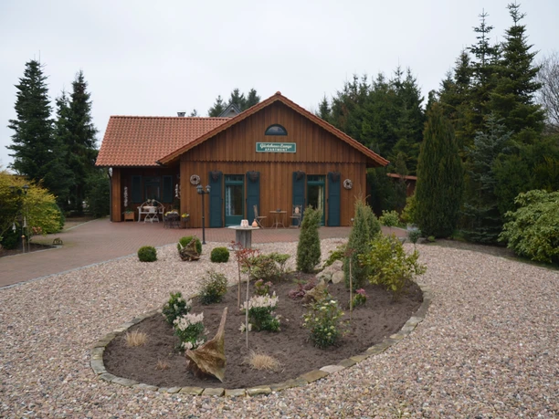 An inviting wooden guest house with plant beds and brick path, surrounded by tall trees.