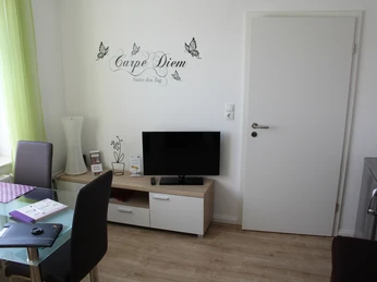Gästezimmer Bär Helles Gästezimmer mit moderner Einrichtung, Wandtattoo "Carpe Diem" über TV, helle Vorhänge.
