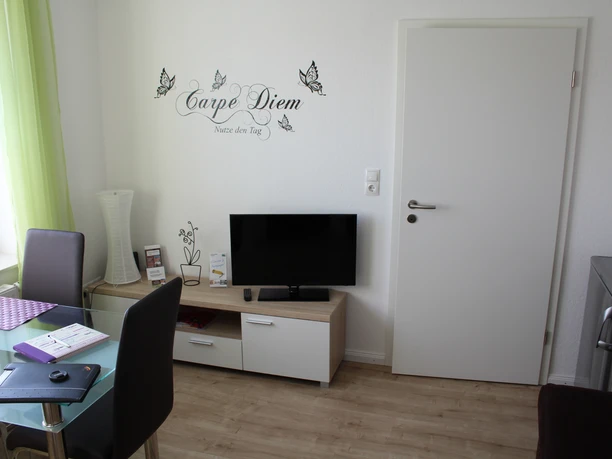 Gästezimmer Bär Helles Gästezimmer mit moderner Einrichtung, Wandtattoo "Carpe Diem" über TV, helle Vorhänge.