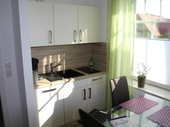 Gästezimmer Bär Helles Gästezimmer mit moderner Küchenzeile, Essbereich, Tageslicht und Blick auf rote Dachziegel.