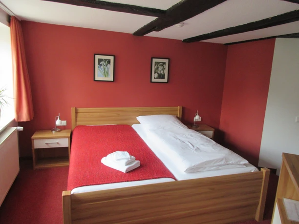 Hotel Ambiente Nienburg Doppelzimmer im Hotel mit Holzbett, roten Wänden und Bettläufer, Dachbalken an der Decke.