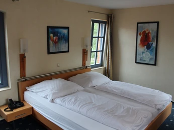 Hotel zum Kanzler Doppelzimmer mit heller Einrichtung, Fenster mit Blick nach draußen und farbenfrohen Kunstwerken an den Wänden.